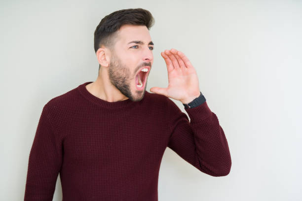 istock Young handsome man wearing a sweater over isolated background shouting and screaming loud to side with hand on mouth. Communication concept. 1124771003
