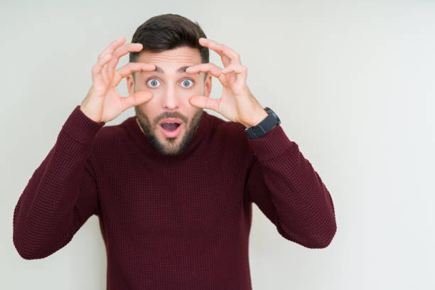 Young handsome man wearing a sweater over isolated background Trying to open eyes with fingers, sleepy and tired for morning fatigue