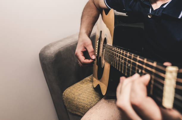 istock Man at home is playing the guitar. Guys hands are taking the chord on strings. Music making lifestyle concept. Free time hobby for everyone. Retro guitar photo. 1124771373