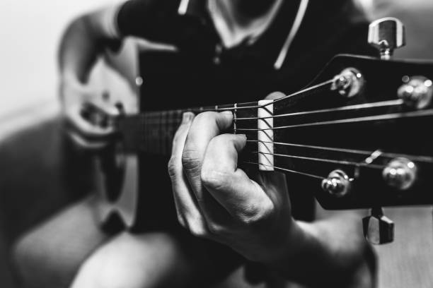 istock Man at home is playing the guitar. Guys hands are taking the chord on strings. Music making lifestyle concept. Free time hobby for everyone. Retro black and white guitar photo. 1124771448