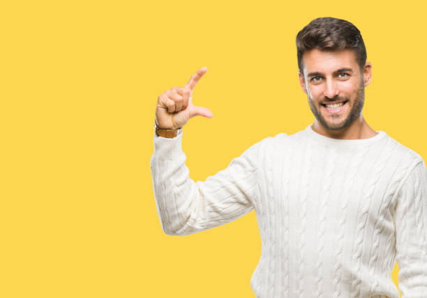 istock Young handsome man wearing winter sweater over isolated background smiling and confident gesturing with hand doing size sign with fingers while looking and the camera. Measure concept. 1124772680