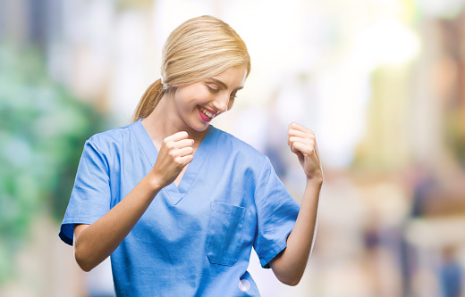 Young beautiful blonde doctor surgeon nurse woman over isolated background very happy and excited doing winner gesture with arms raised, smiling and screaming for success. Celebration concept.
