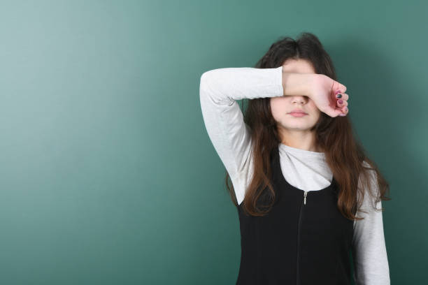 Smiling little schoolgirl on green background . Young playful girl closes her eyes