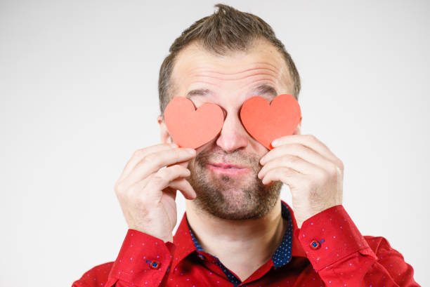 Adult funny man covering eyes with red hearts. Male blinded by love. Romance feelings valentines day concept