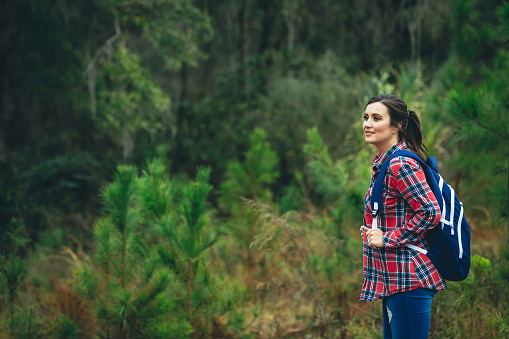 A beautiful woman with long dark hair in a ponytail hiking with her backpack outdoors near and in a forest