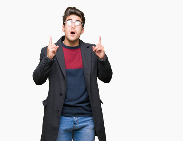 istock Young handsome elegant man wearing glasses over isolated background amazed and surprised looking up and pointing with fingers and raised arms. 1124797144