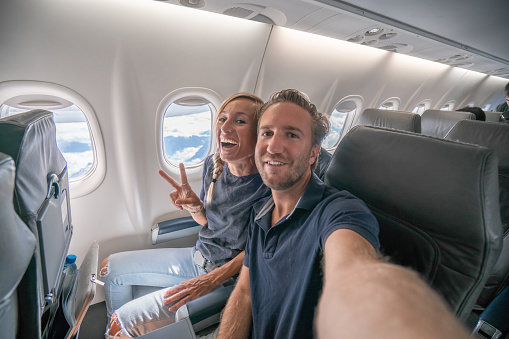 Young couple in airplane using mobile phone during flight to take selfie portrait \nPeople travel technology concept