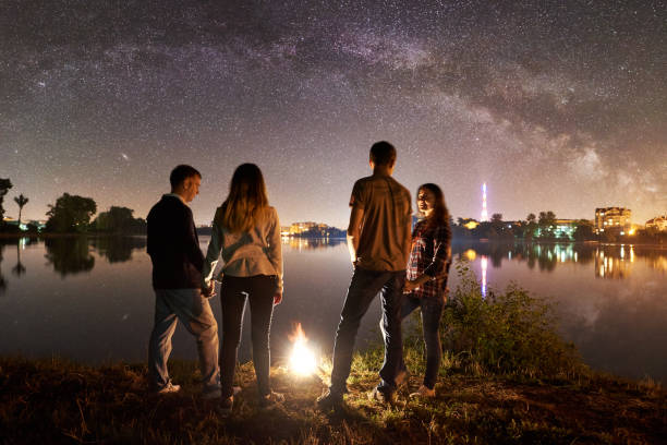 istock Two couple resting on lake shore near fire at night camping 1124801545