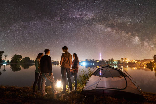 istock Two couple resting on lake shore near fire at night camping 1124801590