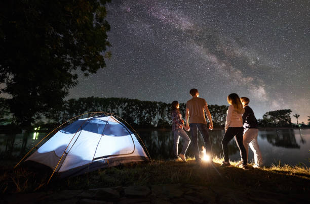 istock Two couple resting on lake shore near fire at night camping 1124801628