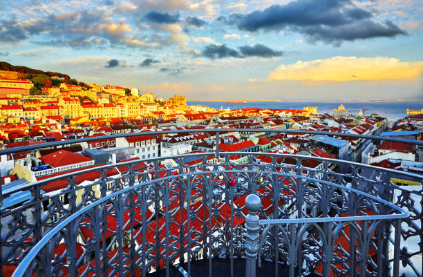 Panorama of Lisbon, from Santa Justa Lift Panorama of Lisbon, Portugal. View from Santa Justa Lift viewing platform at Alfama district old town and sea far away. Evening sunset with dramatic sky. Famous touristic destination landmark. santa justa lift portugal stock pictures, royalty-free photos & images