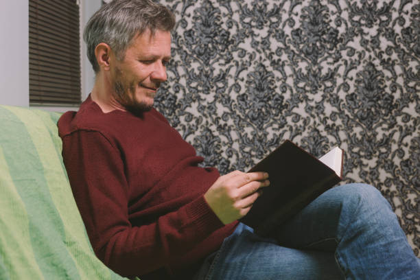 istock Beautiful adult man sitting on sofa, enjoy reading book 1124815020
