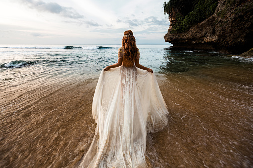 Bride in a white wedding dress comes into the sea water on the beach