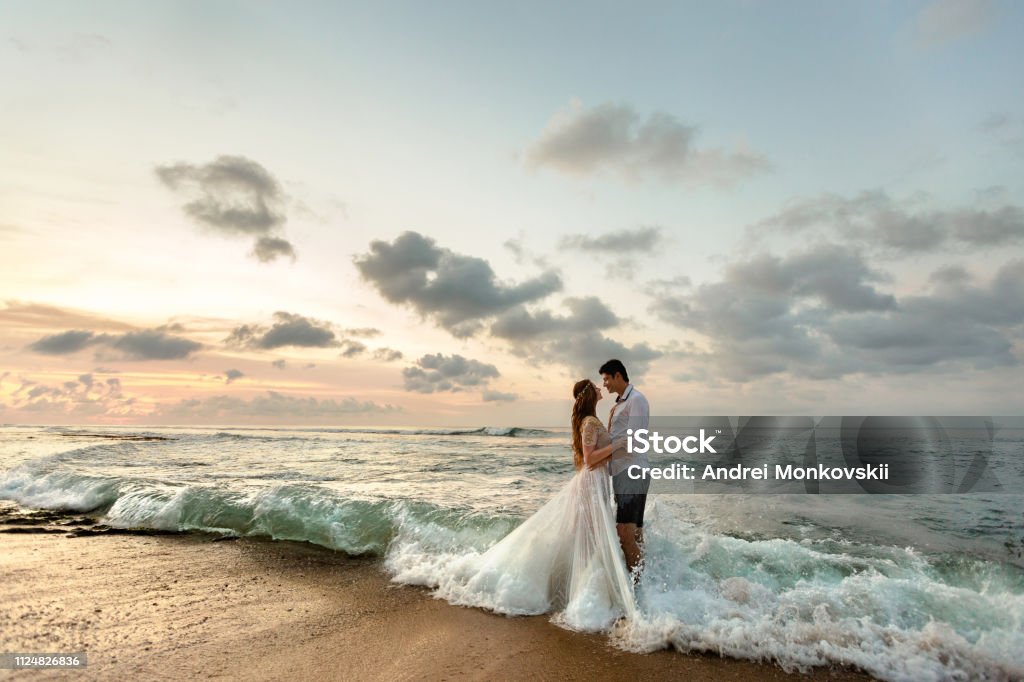 Newlyweds on the beach at sunset Bride and groom hugging on the beach standing in the sea water Wedding Stock Photo