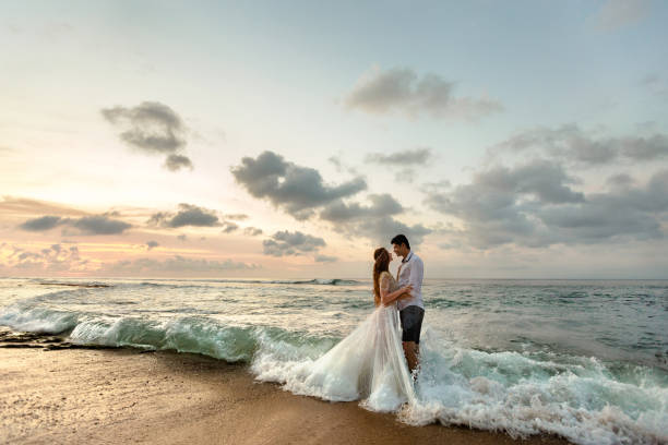 Newlyweds on the beach at sunset Bride and groom hugging on the beach standing in the sea water beautiful bride stock pictures, royalty-free photos & images