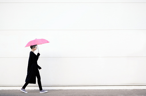 Young woman in black clothes walking with pink umbrella
