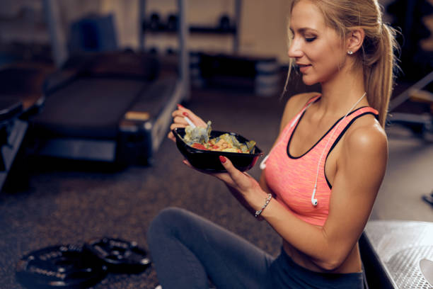 vue latérale d’une femme manger une nourriture saine dans une salle de sport. - healthy eating sport exercising women photos et images de collection