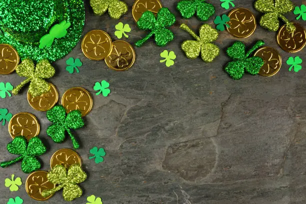 Photo of St Patricks Day corner border of shamrocks, gold coins & leprechaun hat over a dark background