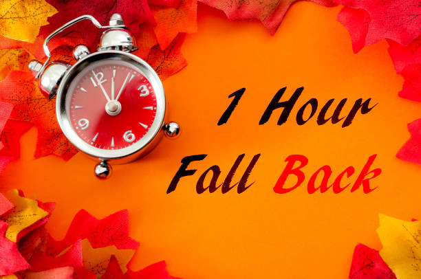 istock Fall back, the end of daylight savings time and turn clocks back on hour concept with a clock surrounded by dried yellow leaves with the text One hour fall back 1124866708