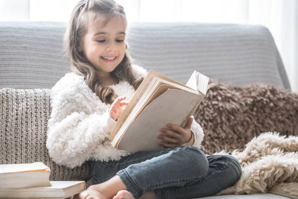 istock little girl reading a book on a comfortable sofa, beautiful emotions 1124869900