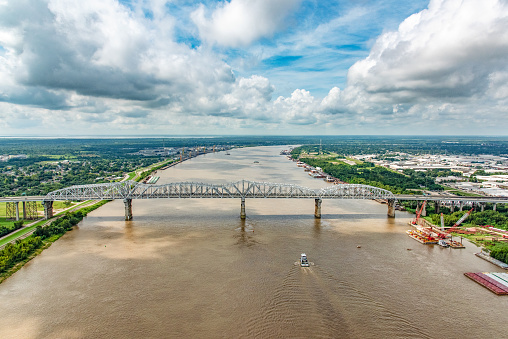 A bridge supporting both vehicles and a railway crossing the Mississippi River which is flanked on both sides by various industry located just north of New Orleans, Louisiana, shot from an altitude of about 600 feet over the river.