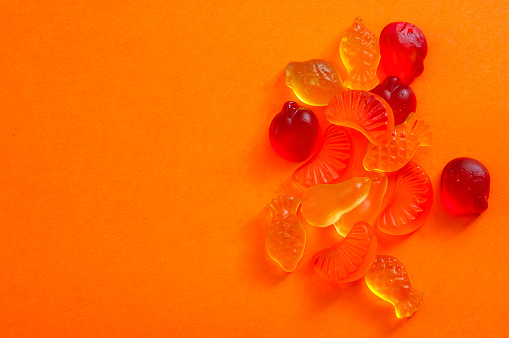 Unhealthy eating and gelatin-based chewable sweets concept with close up on a bunch of colorful fruit shaped gummy candy or jelly candies isolated on orange background with copy space