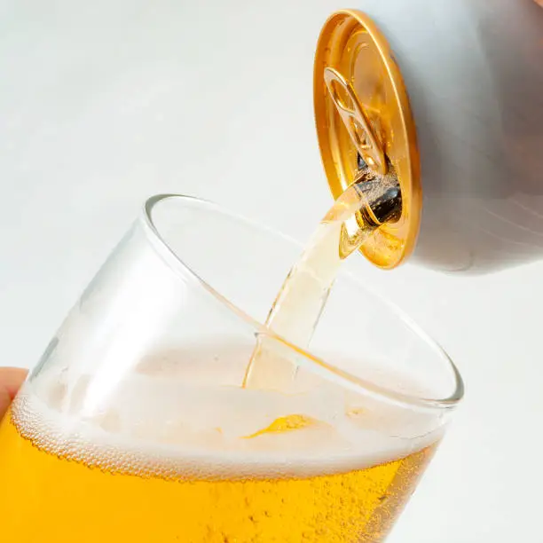 Photo of Alcoholic beverage, drinking alcohol and alcoholic content concept with close up on a hand pouring from a can of beer into a clear glass isolated on white background