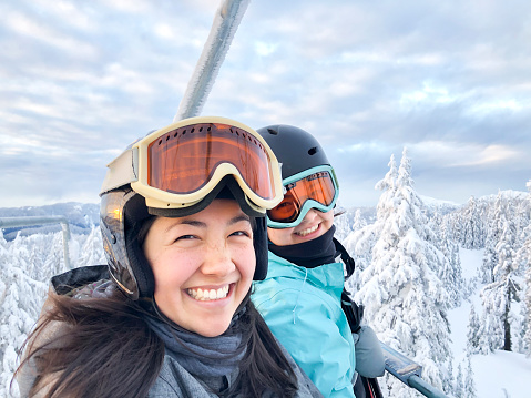 Mobile phone photo.  Eurasian sisters in ski gear, riding chairlift.  Mt. Seymour, North Vancouver, British Columbia, Canada.