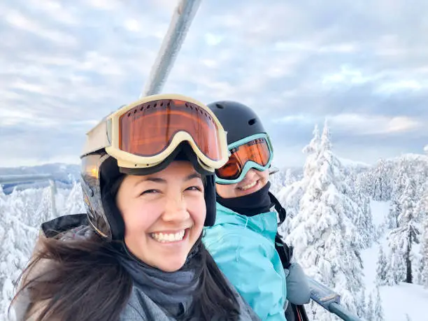 Photo of Portrait of Multi-Ethnic Sisters Riding Chairlift, Ski Runs in Background