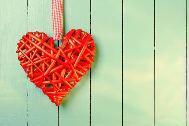 Red wicker heart on a green painted wooden background. Space for copy.