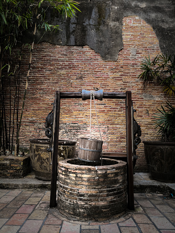 Ancient artesian well  with hanging wood bucket and wooden roof on brick wall background.