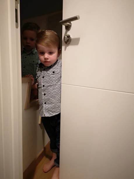 istock toddlers mischief, hiding behind door 1124989409