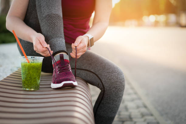 green detox smoothie cup and woman lacing shoes before workout. - shoe tying adult jogging imagens e fotografias de stock