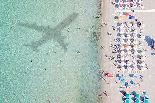 Aerial view of the amazing beach with the shadow of an airplane and people who swim.