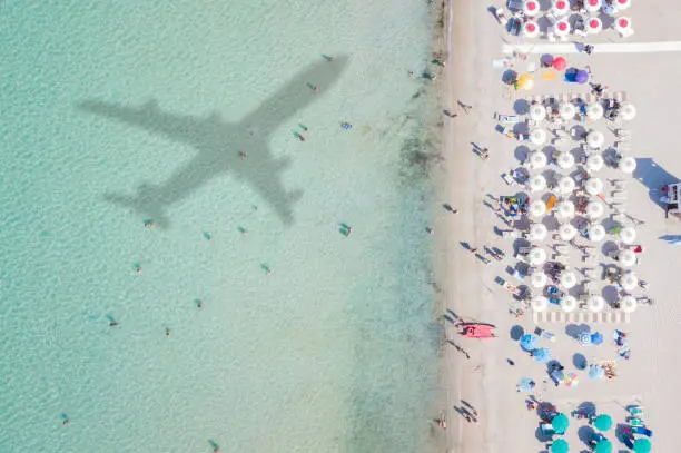 Photo of Aerial view of the amazing beach with the shadow of an airplane and people who swim.
