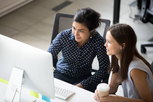 multiracial colleagues sitting together looking at laptop screen in office - trainee imagens e fotografias de stock