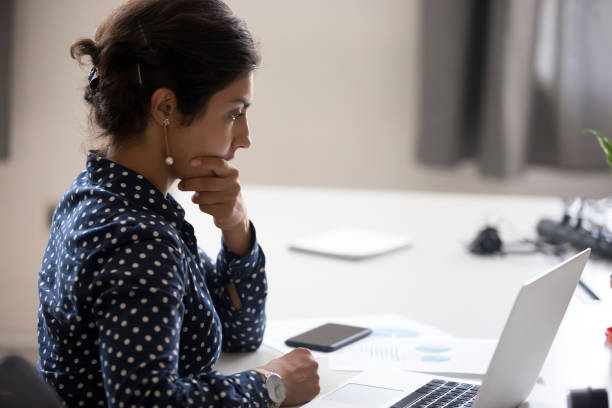 Concentrated serious office worker millennial woman analysing results Indian girl sitting at desk near computer cogitating thinking making important decision at workplace. Concentrated serious office worker millennial woman analysing results feels doubts and feel unsure determination asian stock pictures, royalty-free photos & images