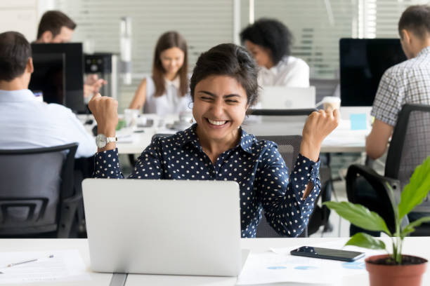 istock Excited woman sitting at desk looking at computer screen 1124997373