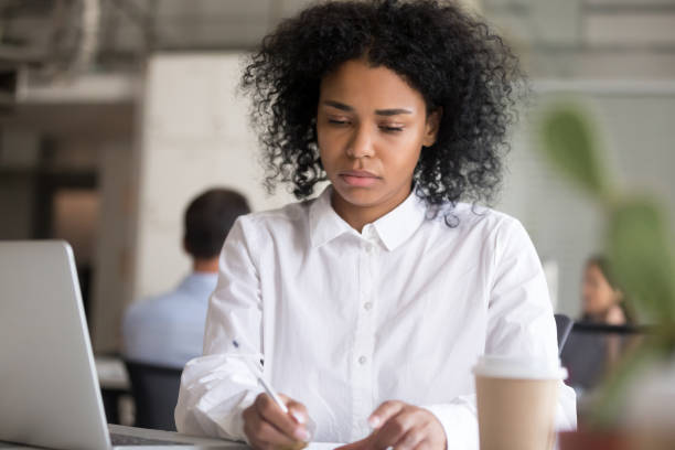 istock Serious black woman writing note sitting at desk in work 1124997387