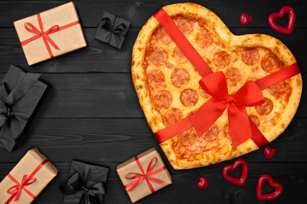 istock Pizza pepperoni shaped heart with red ribbon bow and present box for Valentine's Day on rustic dark black background. Top View. Flat lay 1124998730