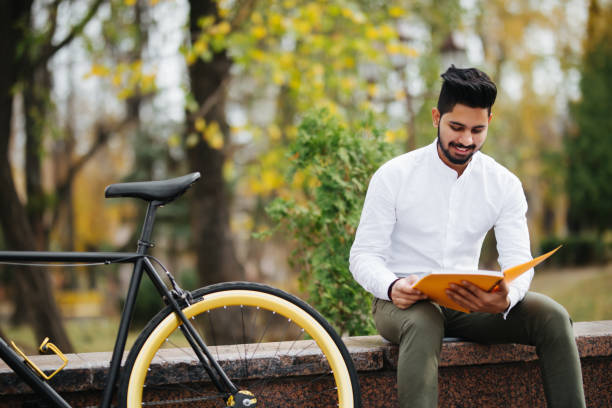 istock Young indian man reading a book while taking a break on the city street 1125007754
