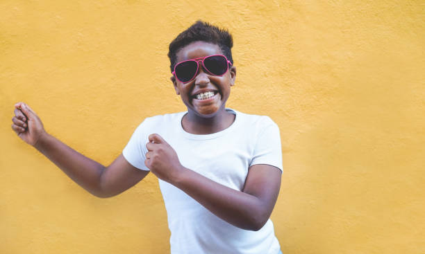 african male child dancing outdoor wearing sunglasses - black afro kid having fun with yellow background - focus on face - youth lifestyle, trendy , fashion and happiness concept - child caribbean black latin american and hispanic ethnicity imagens e fotografias de stock