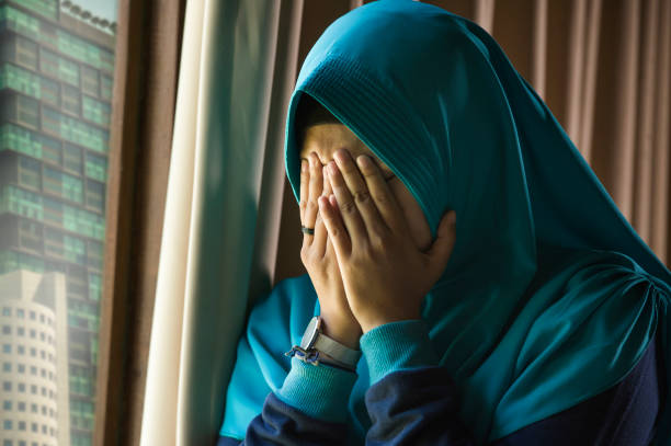lebensstil-porträt des jungen traurig und deprimiert muslimin im islam traditionelle hijab kopftuch an home-fenster gefühl krank leiden depression-krise und angst problem schreit hilflos - southeast asia fotos stock-fotos und bilder