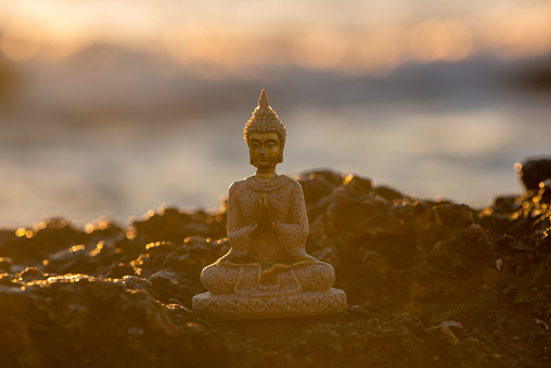 Figure of a buddha meditating by the sea at sunrise, Spain