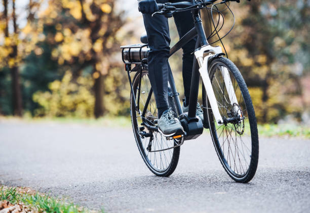 un uomo irriconoscibile in electrobike in bicicletta all'aperto su una strada nel parco. - bicicletta elettrica foto e immagini stock