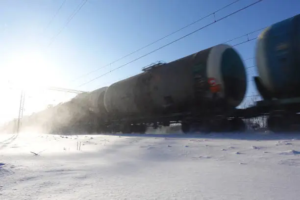 Photo of Freight train with oil tanks in motion. Snow dust flies from a passing train at high speed. Frosty sunny day. Winter. Russia.