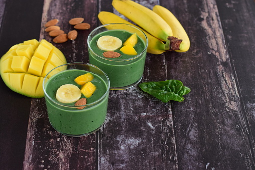 Green smoothie with spirulina, spinach, banana, mango and almond on dark wooden background