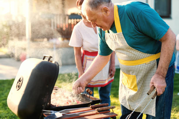 istock Grandparents with aprons grilling meat and vegetables on sticks while standing in backyard at spring. 1125018091