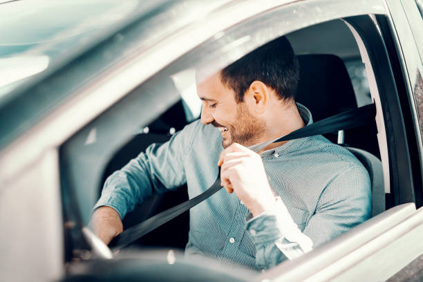 ritratto di uomo caucasico sorridente che fissa la cintura di sicurezza e si siede nella sua auto. finestra aperta, vista laterale. - car driving men business foto e immagini stock