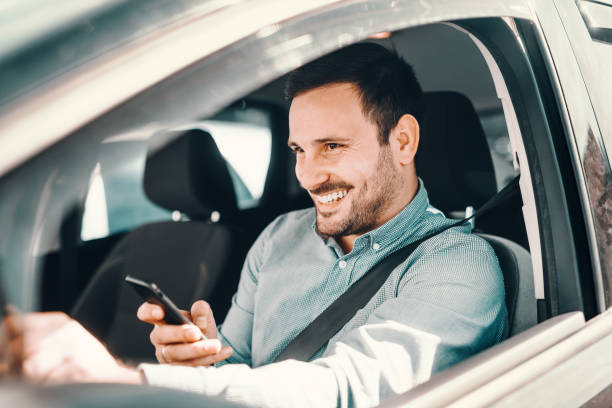 istock Close up of smiling bearded man using smart phone for writing or reading message with hand on the steering wheel. 1125024669